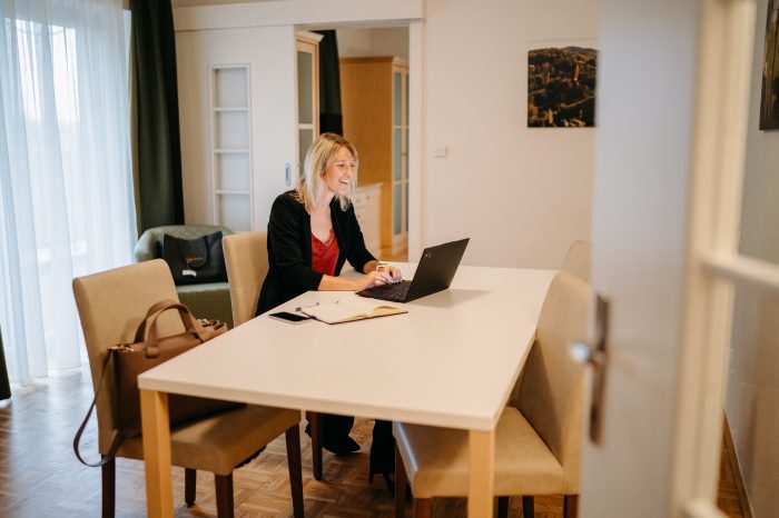 Ein Businessgast sitzt am Konferenztisch in der Businesssuite am Laptop und lächelt.