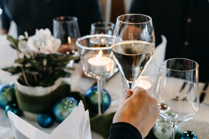 Ein Glas Sekt, im Hintergrund ein weihnachtlicher gedeckter Tisch.