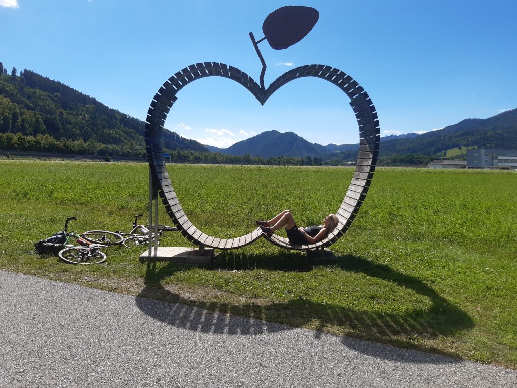 Eine Radfahrerin liegt in einer riesigen Apfelliege mit Blick in die weite den Hügellandes. Daneben liegen 2 Gravelbikes.