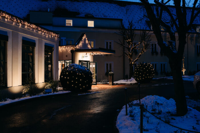 Der Eingangsbereich vom Hotel Staribacher in der Südsteiermark mit Weihnachtsbeleuchtung und Schnee bei Nacht.