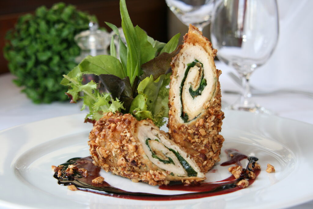 Winterkulinarik. Gourmetspeise: Eine knusprige Hühnerroulade mit einer dunkelroten Sauce und einer Salatdekoration.