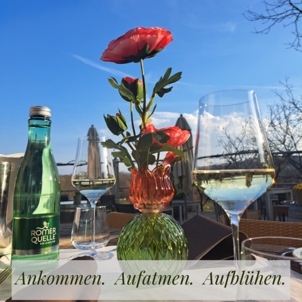 Gedeckter Tisch auf der Terrasse vom Hotel Staribacher Südsteiermark mit Wein, Blumen und Blick in den blauen Frühlingshimmel.